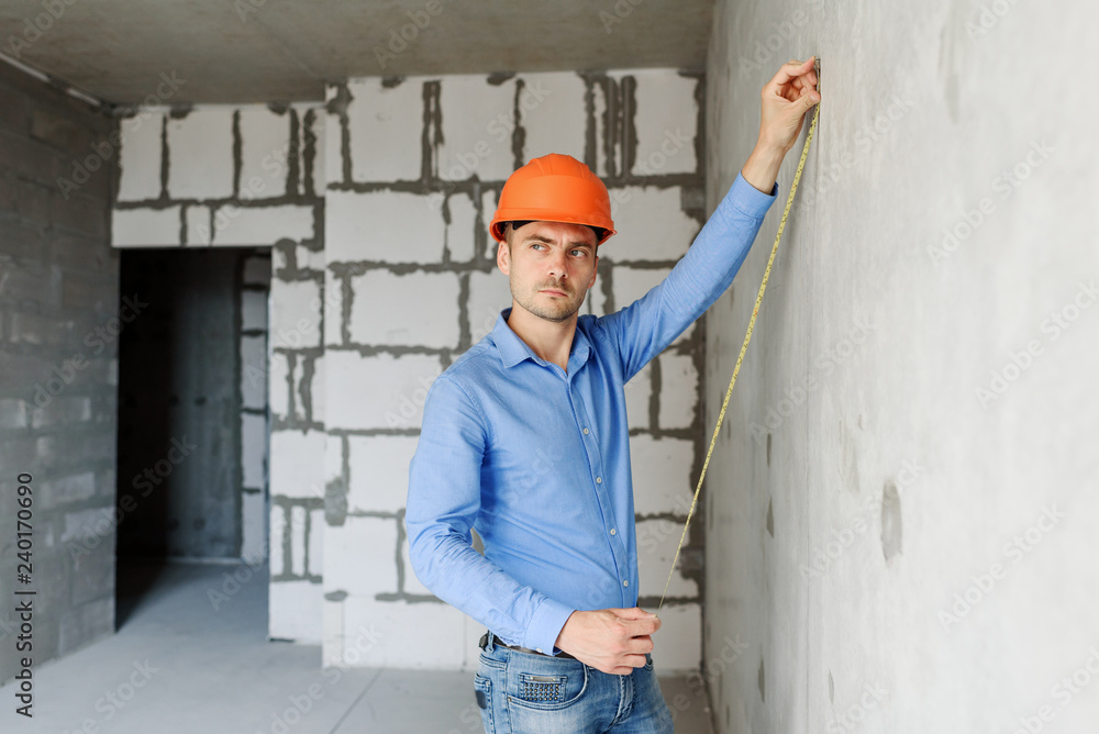 Satisfied construction worker foreman measures a tape measure of a wall parameter in a house under construction. Inspects repair readiness and accuracy of work performed Satisfied construction worker foreman measures a tape measure of a wall parameter in a house under construction. Inspects repair readiness and accuracy of work performed