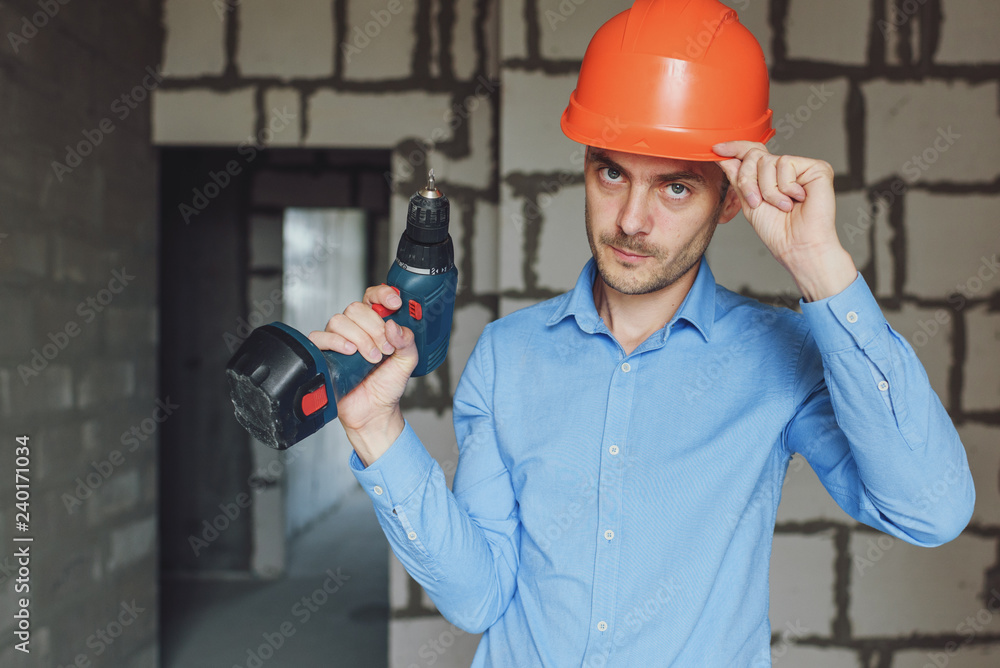 Smiling man with electric drill wearing protective helmet. Repair concept Smiling man with electric drill wearing protective helmet. Repair concept