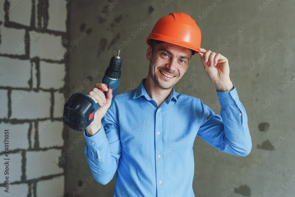 Smiling man with electric drill wearing protective helmet. Repair concept Smiling man with electric drill wearing protective helmet. Repair concept
