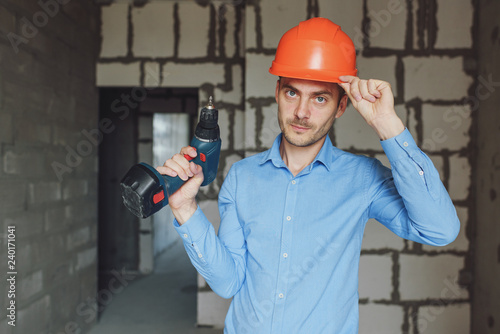 Smiling man with electric drill wearing protective helmet. Repair concept