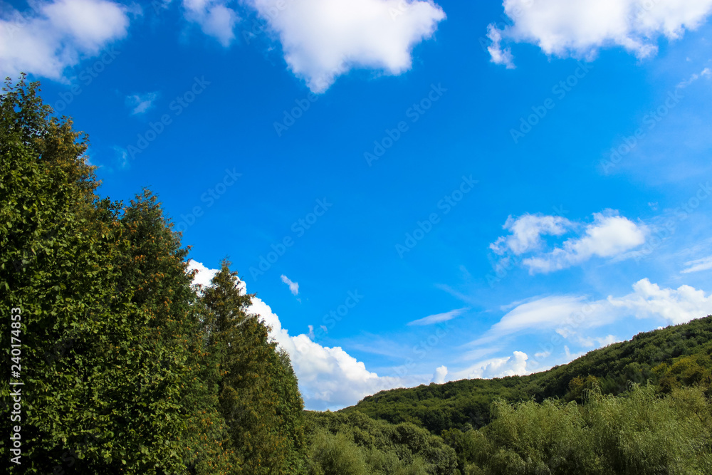 Beautiful white clouds against the background of a beautiful blue sky and green forest on hills