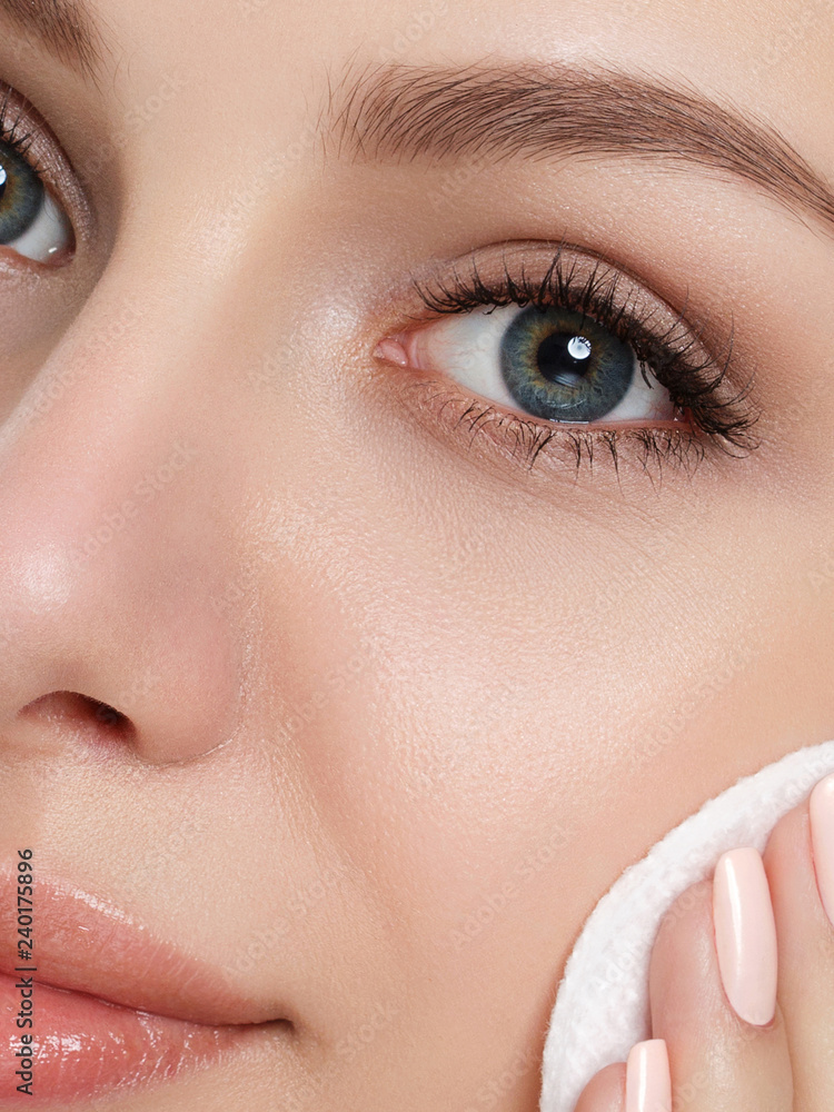 Fototapeta premium Portrait of young beautiful woman with towel on her hair cleaning makeup from her face with cosmetic pad isolated over white background. Cleaning face, perfect skin, skincare and cosmetology concept
