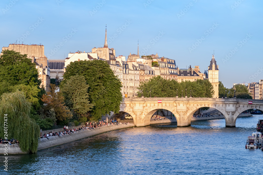 Cite island and Pont Neuf in Paris on a sunny summer. People are sitting on the river bank.