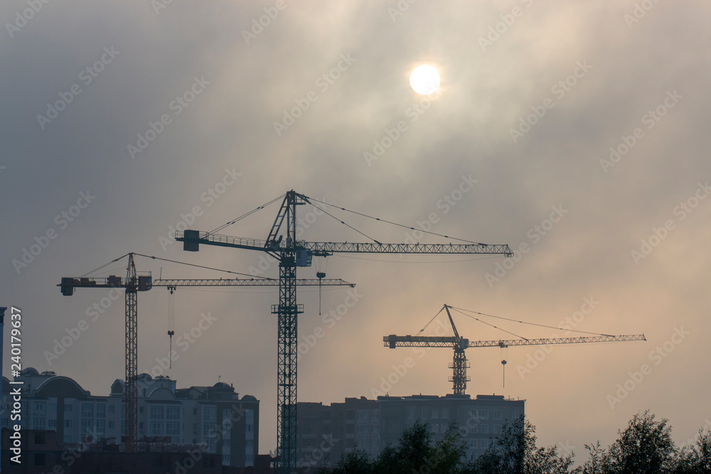 very high construction crane in the morning fog, against the gray sky background