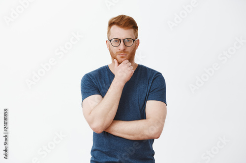 Creative and smart businessman thinking about new concept for business. Portrait of handsome strategist with red hair and bristle, holding hand on beard and staring at camera focused