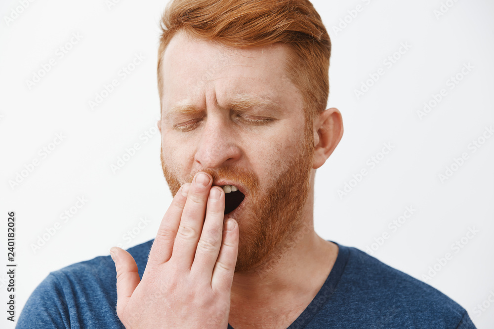 Headshot of tired attractive male entrepreneur with red hair and beard, yawning with closed eyes, covering opened mouth with palm, feeling tired, sleepy after taking nap or waking up early in morning Headshot of tired attractive male entrepreneur with red hair and beard, yawning with closed eyes, covering opened mouth with palm, feeling tired, sleepy after taking nap or waking up early in morning
