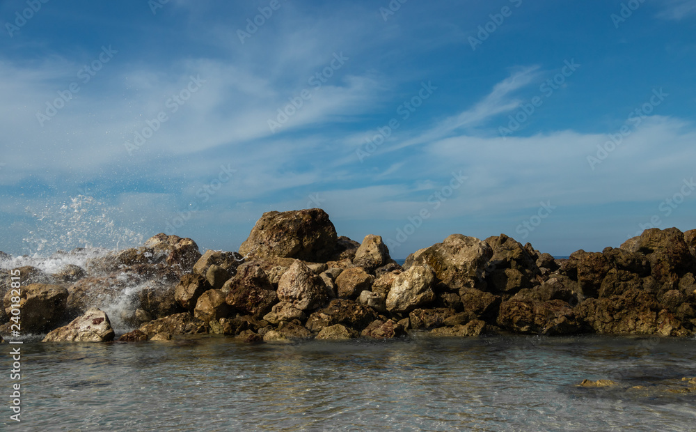 Ocean waves break over a rock wall sending spray into the air. Bright blue sky and clear turquoise water of an island paradise coastal scene. Ocean waves break over a rock wall sending spray into the air. Bright blue sky and clear turquoise water of an island paradise coastal scene.