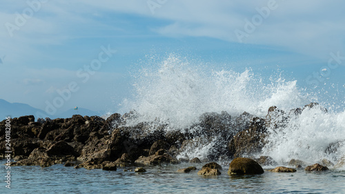 Ocean waves break over a rock wall sending spray into the air. Bright blue sky and clear turquoise water of an island paradise coastal scene.