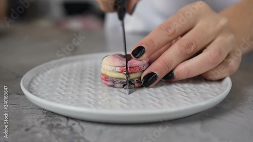 Close up shot of woman hands cutting macaroon on the halves using knife. photo