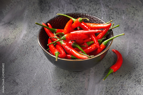 Closeup on red hot chili peppers in ceramic bowl over dark textured table