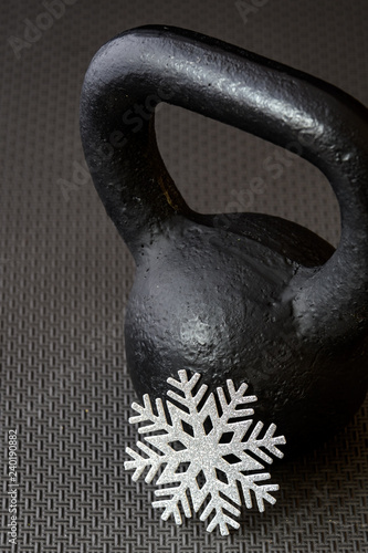 Black kettlebell on a black gym floor with a silver snowflake to celebrate winter fitness