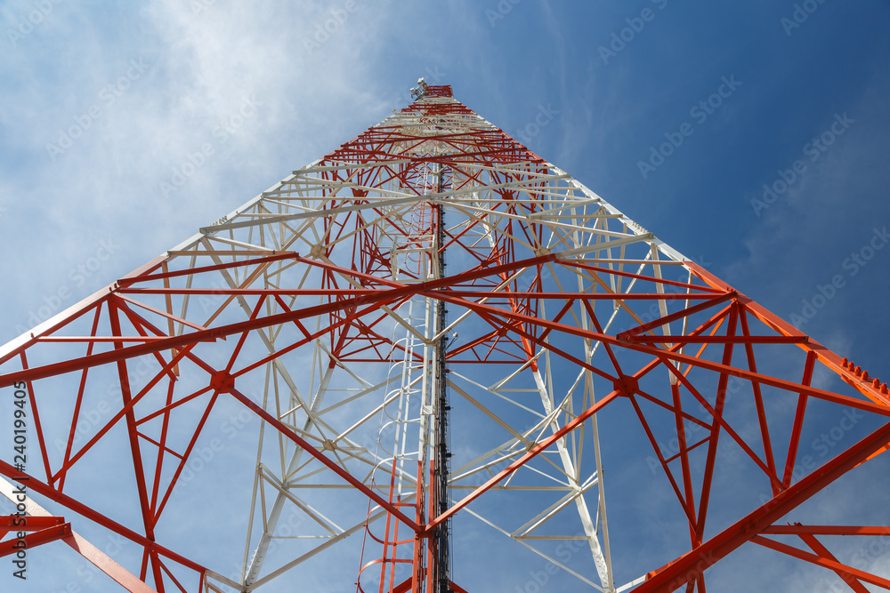 bottom view of a telecommunications tower. red and white cell phone tower against blue sky, view at the base