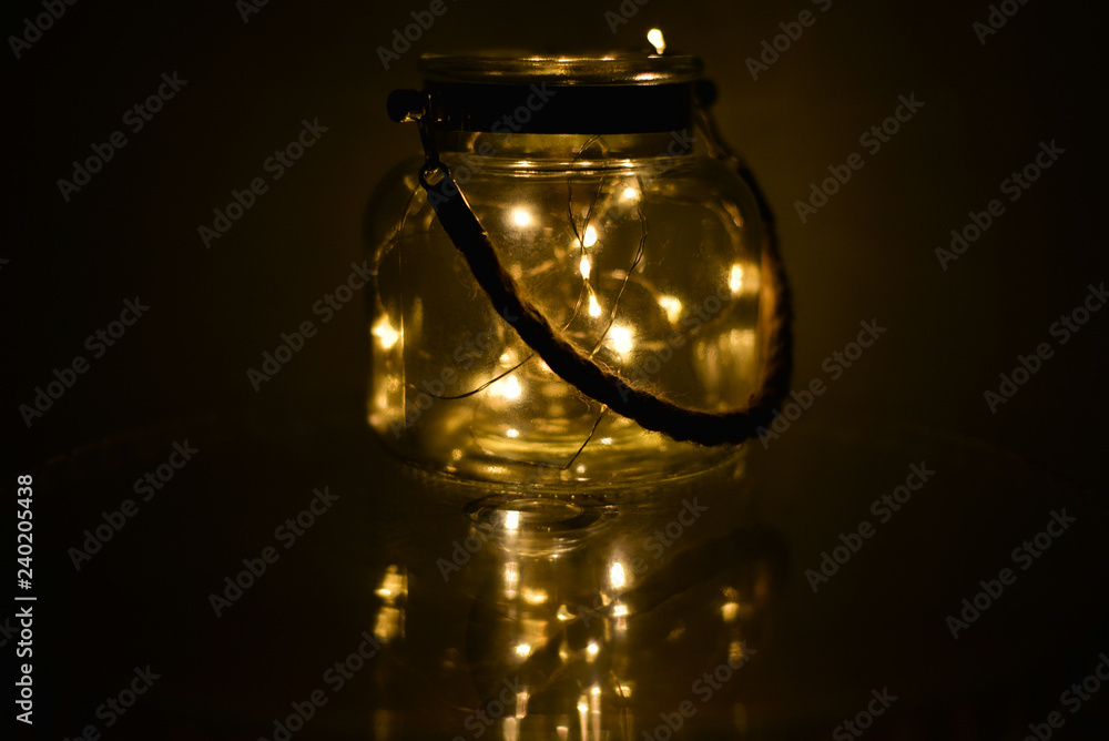 Decorative lights in glass jar at the dark room with mirror effect on dark background. Festive decorations .Warm white led lights