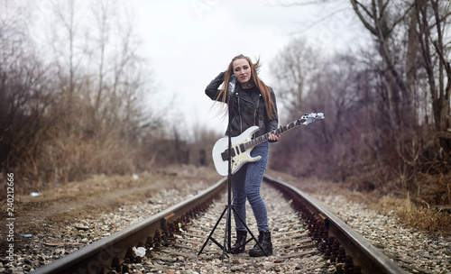 Beautiful young girl rocker with electric guitar. A rock musician girl in a leather jacket with a guitar sings. A rock band soloist plays the guitar and screams into the microphone.