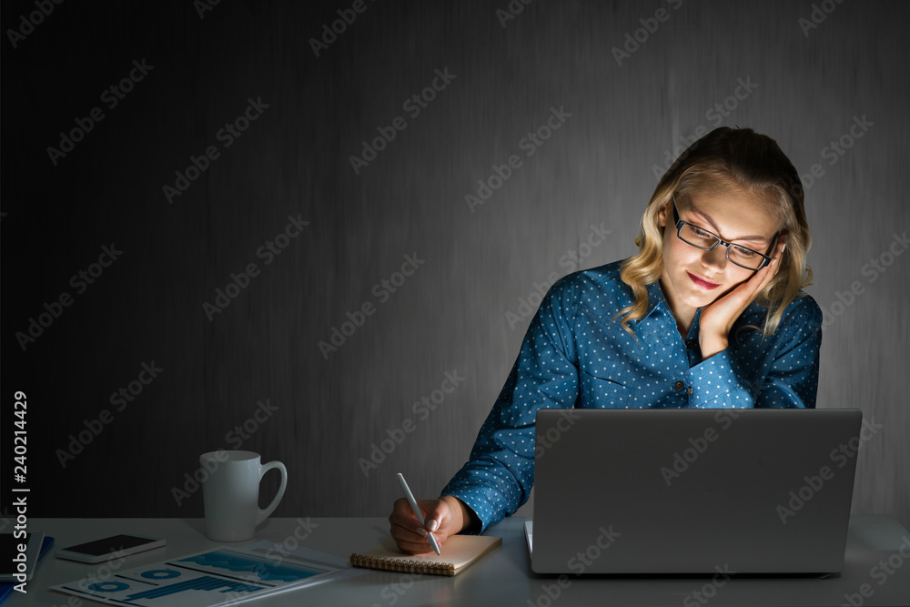 Attractive blonde working on laptop in dark office. Mixed media Attractive blonde working on laptop in dark office. Mixed media
