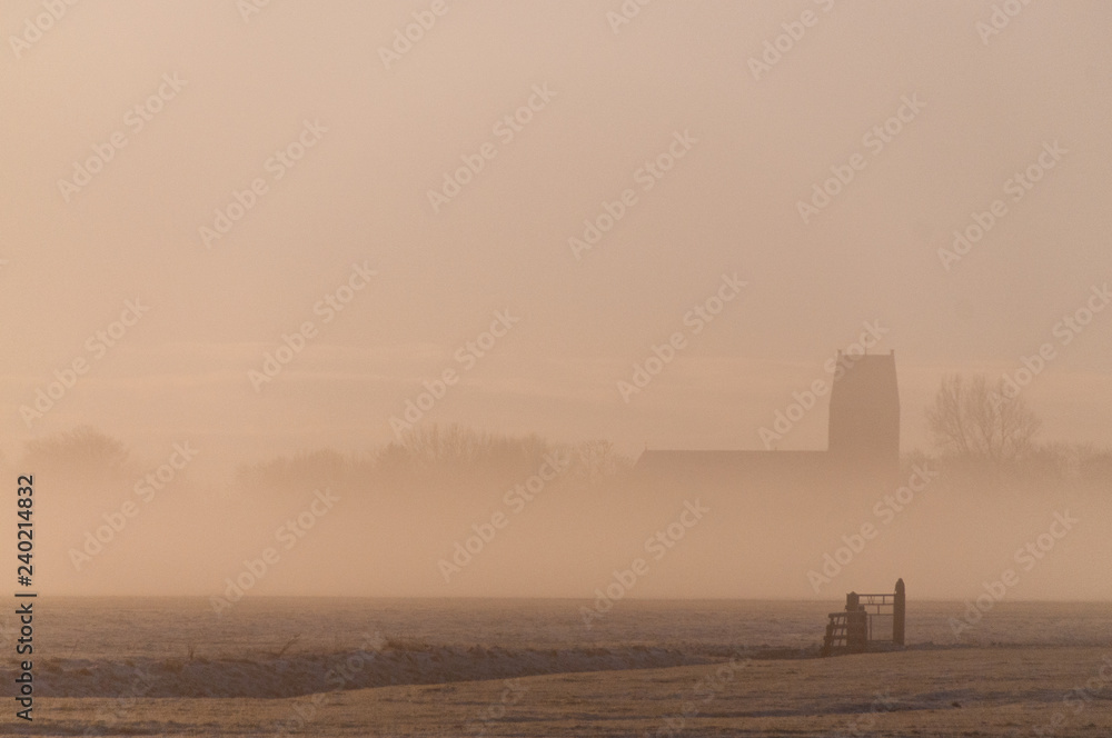 A mist covered landscape showing the 14th century Petrus church in the town of Wanswerd, on a rare white christmas morning.