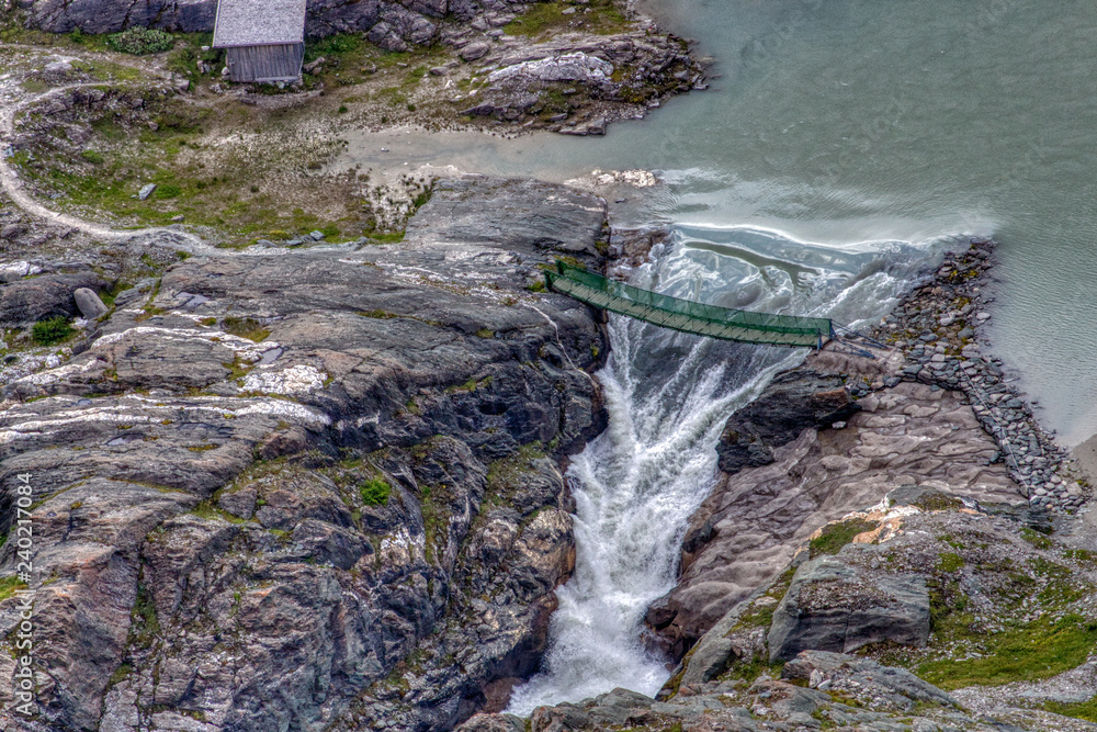 Brücke über Wasserfall an Bergsee mit Felsen und Steinen