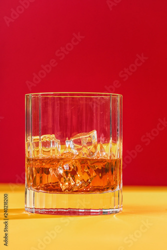 glass of whiskey and ice on red background vertical