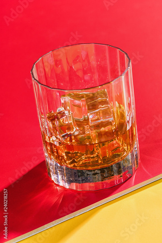 glass of whiskey and ice on red background side view vertical