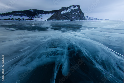 the cross of deep cracks in the thick ice of the winter lake Baikal opposite the rocky mountain of Olkhon Island