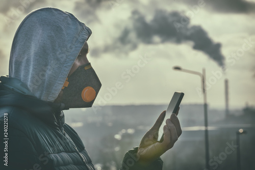 Man wearing a real anti-smog face mask and checking current air pollution with smart phone app