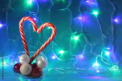 Two Christmas candies in the form of a heart, striped canes, against the background of colored garlands