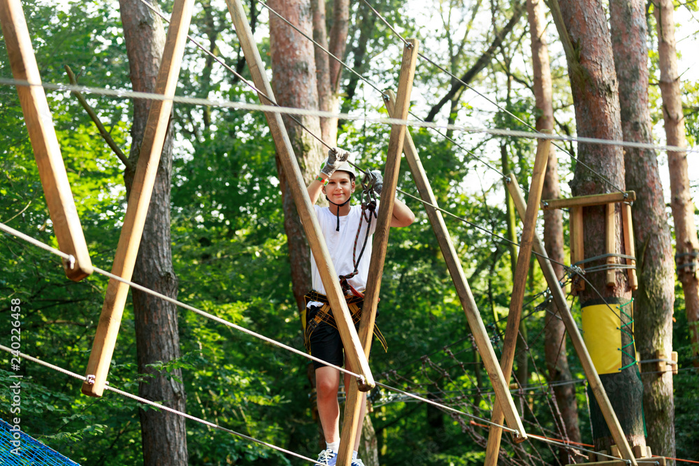 Cute boy enjoying activity in climbing adventure park at sunny summer day. Kid climbing in rope playground structure. Safe climbing with helmet insurance. Child in forest adventure park, extreme sport Cute boy enjoying activity in climbing adventure park at sunny summer day. Kid climbing in rope playground structure. Safe climbing with helmet insurance. Child in forest adventure park, extreme sport