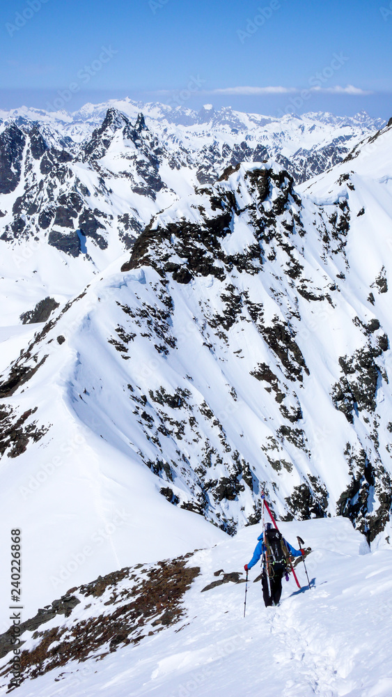 backcountry skier hikes along narrow mountain ridge in the Swiss Alps