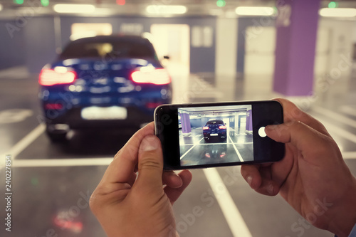 A man is taking a photo of a car on his phone. A toned photo