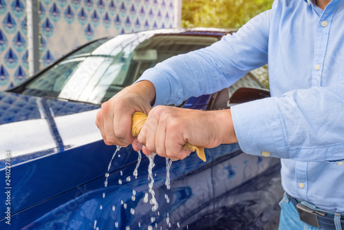 A man’s hands are twisting a wet cloth at the car background.
