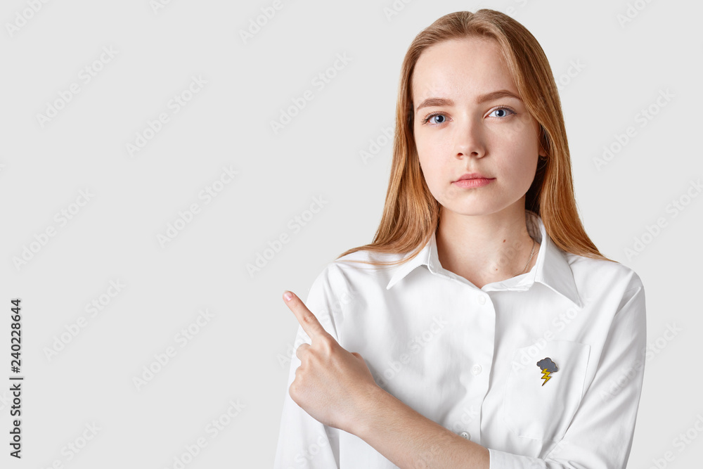 Portrait of confident serious lady has minimal make up, dressed in elegant clothes, points aside up, advertises place with discounts, shows copy space for your promotional content, recommends buy item Portrait of confident serious lady has minimal make up, dressed in elegant clothes, points aside up, advertises place with discounts, shows copy space for your promotional content, recommends buy item