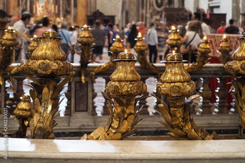 Ornate gold leaf candelabra with flames burning in a chapel in the Vatican City,Rome, with tourists in the background