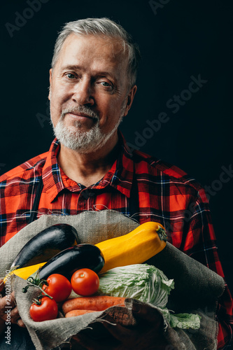 handsome senior gardener with fresh autum vegetables. close up photo. studio shot. isolated black background.food ,farming