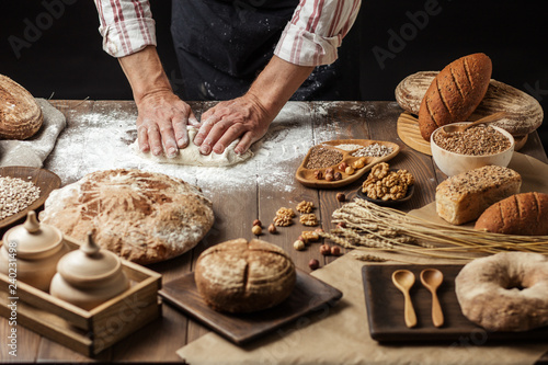 Male Chef kneads the dough with both hands until it becomes elastic, cooking delicious pizza or pastry over studio dark background.