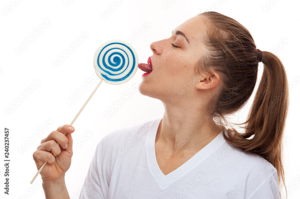 Closeup of modern young woman dressed in white t-shirt loose hair licking lollipop candy on white background Closeup of modern young woman dressed in white t-shirt loose hair licking lollipop candy on white background