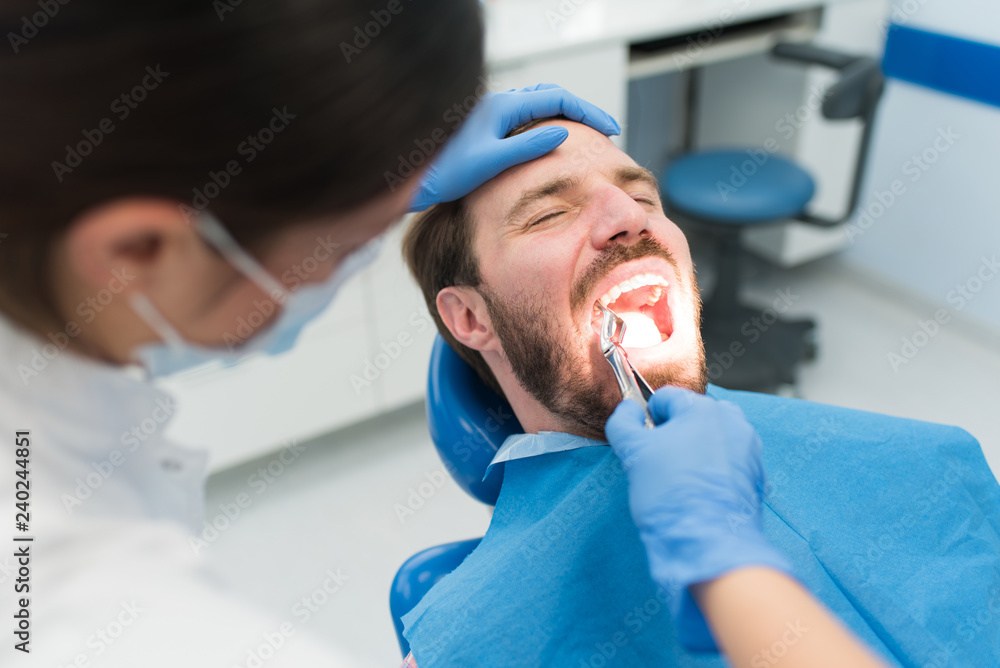 Female dentist pulling teeth out on a male patient with open mouth