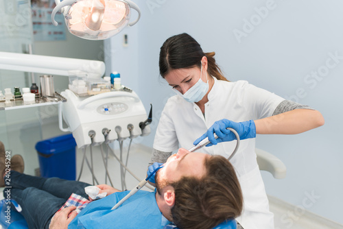 Young female dentist pulling teeth out of a male patient. Painful dental procedure in the dentist office. 