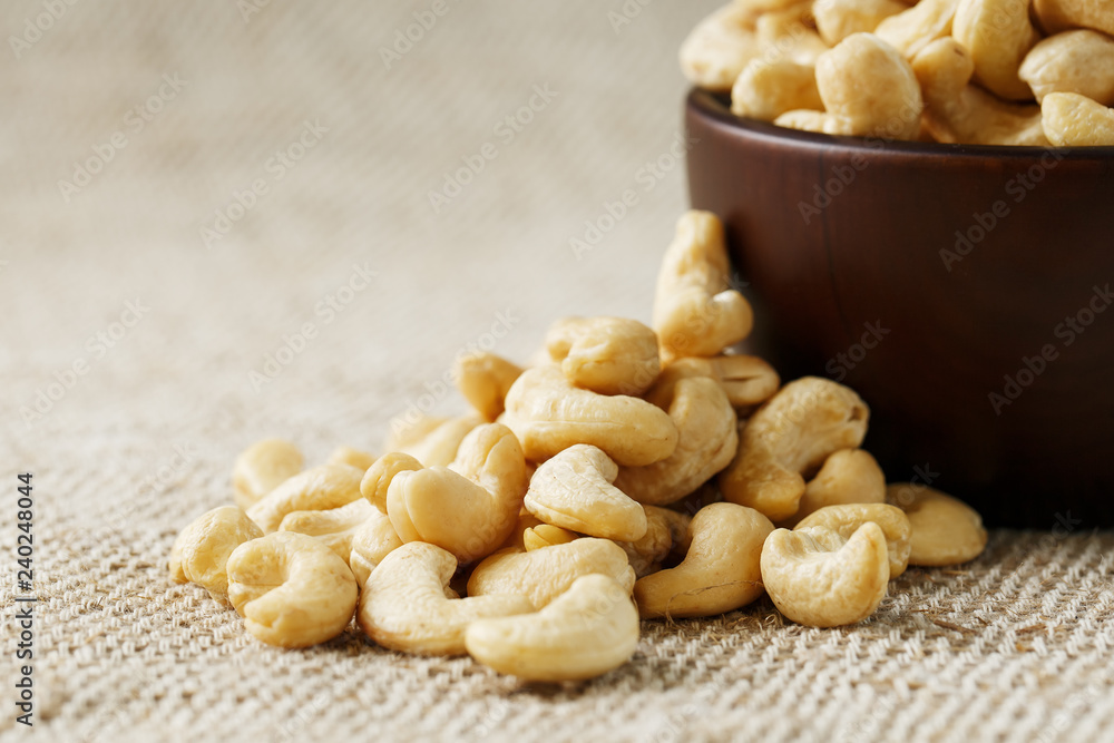 Cashew nuts in a wooden bowl on a burlap cloth background.