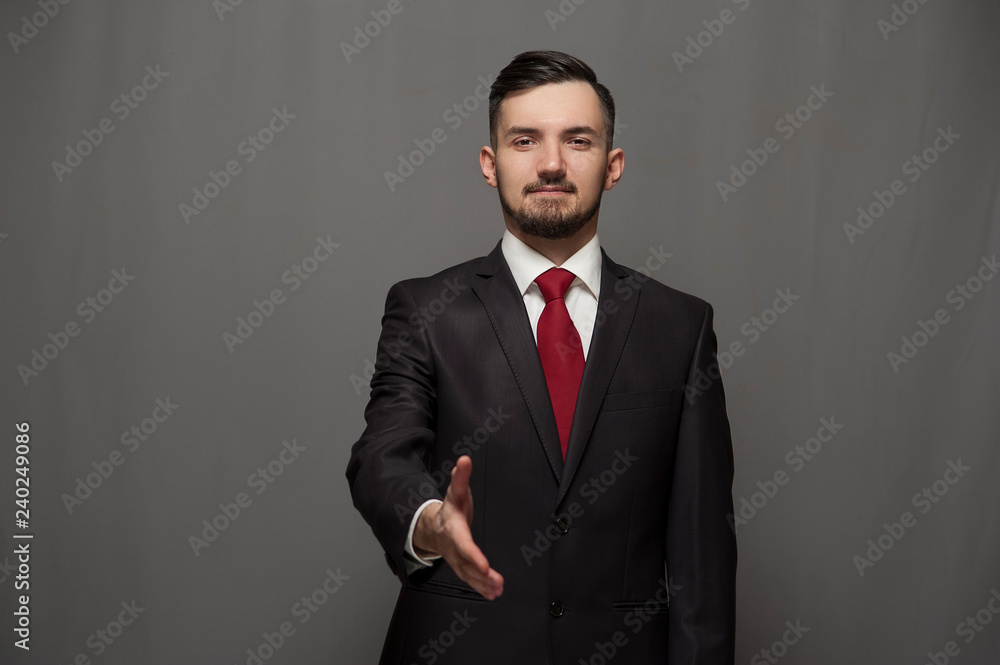 You are our client. Businessman wearing formal suit and glasses holds out his hand for a handshake on gray background You are our client. Businessman wearing formal suit and glasses holds out his hand for a handshake on gray background