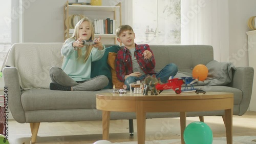 At Home: Cute Girl Playing in Video Game Console, Using Joystick Controller, Her Younger Brothe Cheers for Her. Happy Children Playing Videogames. photo