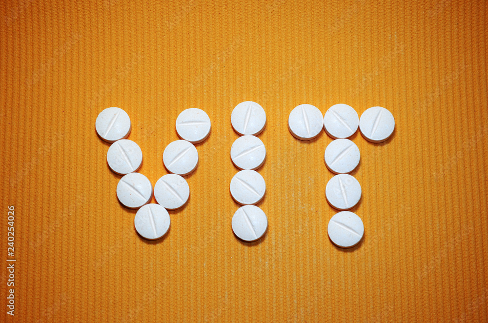 Lots of white smooth convex tablets with dividing strip on yellow striped background, in the form of word VIT, vitamins, top view Lots of white smooth convex tablets with dividing strip on yellow striped background, in the form of word VIT, vitamins, top view