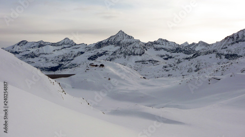 winter mountain landscape with a large mountain hut on a hill next to a dam and reservoir in the Austrian Alps