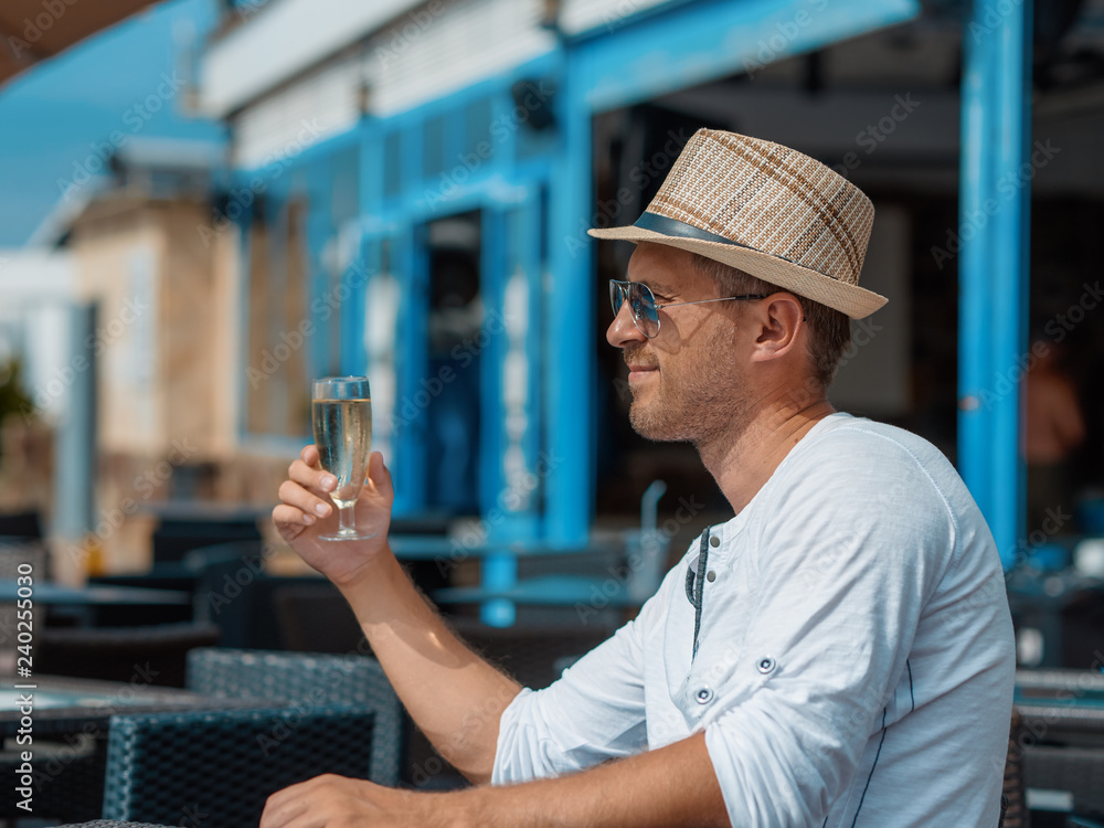 European man in sunhat is sitting at the city café and drinking champagne. He is celebrating something. European man in sunhat is sitting at the city café and drinking champagne. He is celebrating something.