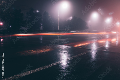 Night foggy street. On the asphalt reflection from passing cars.