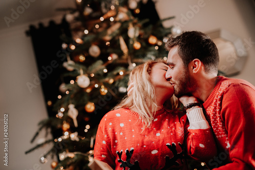 Lovely couple enjoying christmas and opening presents. Couple kissing in front of the christmas tree