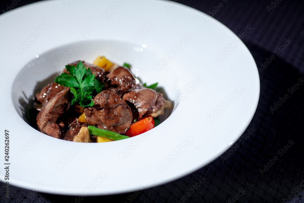 chicken liver in a white plate with vegetables and herbs on a dark background