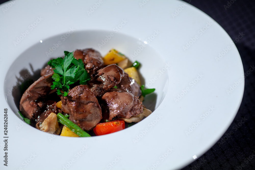 chicken liver in a white plate with vegetables and herbs on a dark background chicken liver in a white plate with vegetables and herbs on a dark background