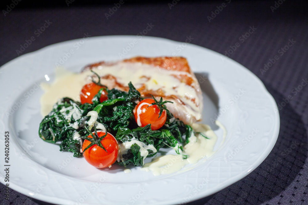 red fish sauce on a white plate on a black background with stewed greens and red tomatoes red fish sauce on a white plate on a black background with stewed greens and red tomatoes