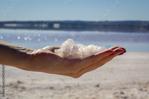 Female hand holding natural salt crystals on the background of a salt lake, side view close up