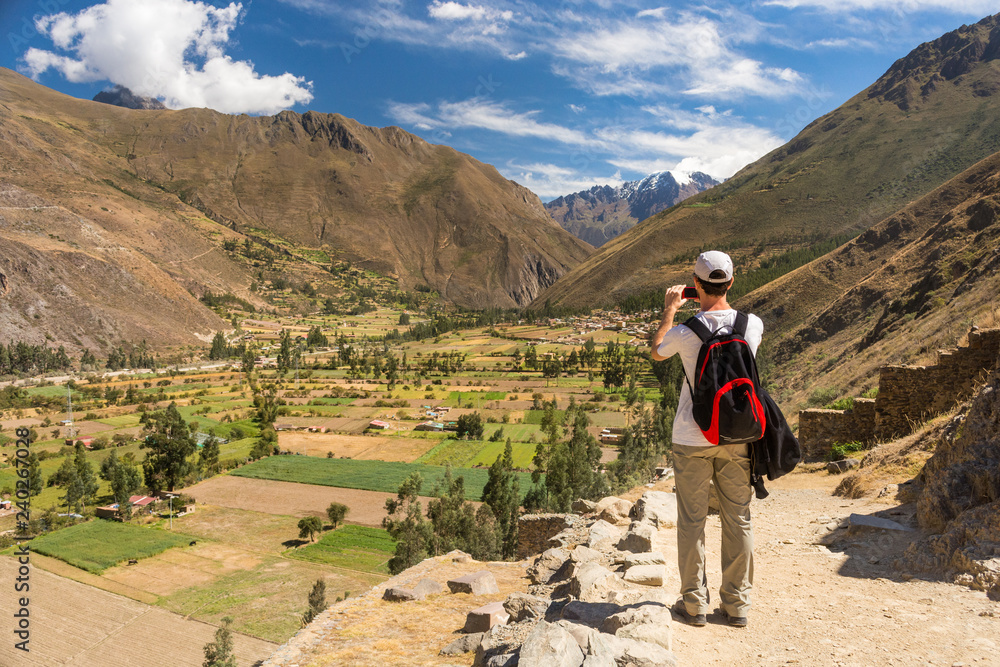 Ollantaytambo, Cusco / Peru - June 9 2017: young man, a tourist, taking a picture of Ollantaytambo valley from the ancient ruins, with an amazing view to the mountains,on an incredible clear sunny day